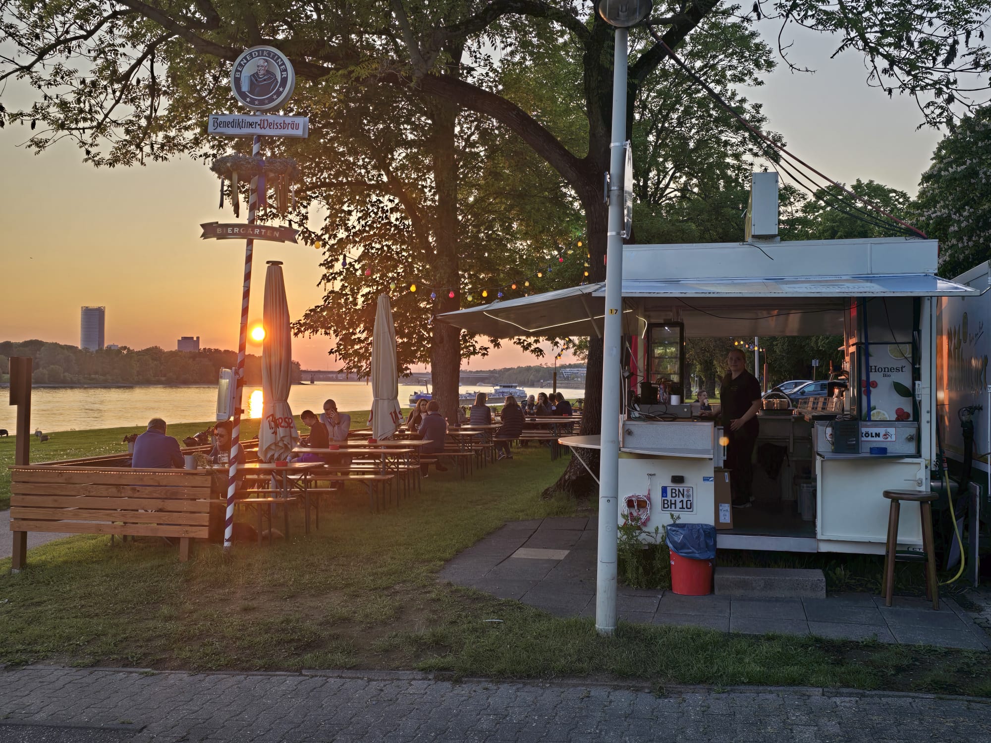 Selbstbedienungsausgabe und Sitzplätze im Biergarten am Rhein bei Sonnenuntergang