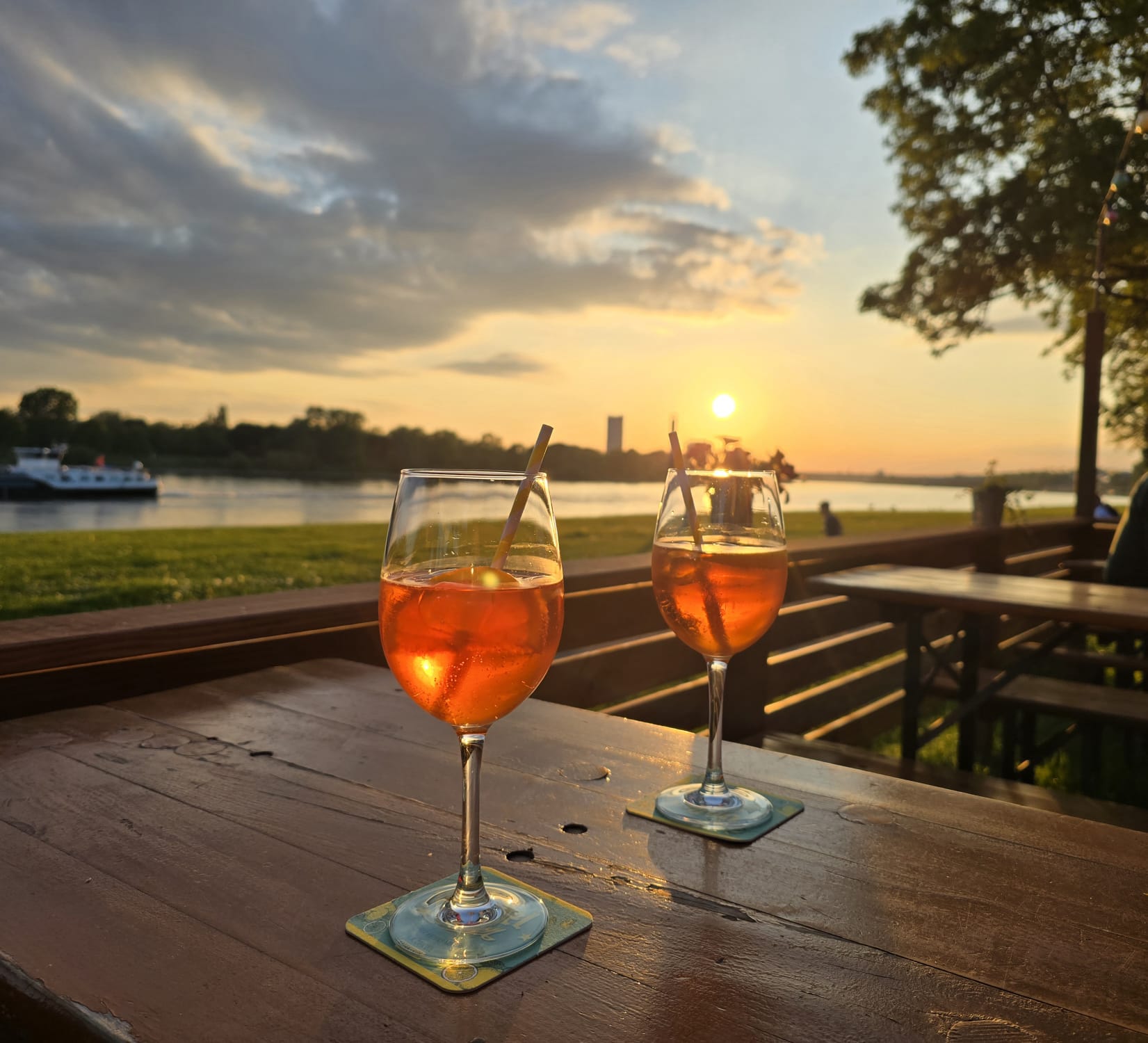 Zwei Getränke auf einem Biergartentisch vor dem Rhein im Abendlicht