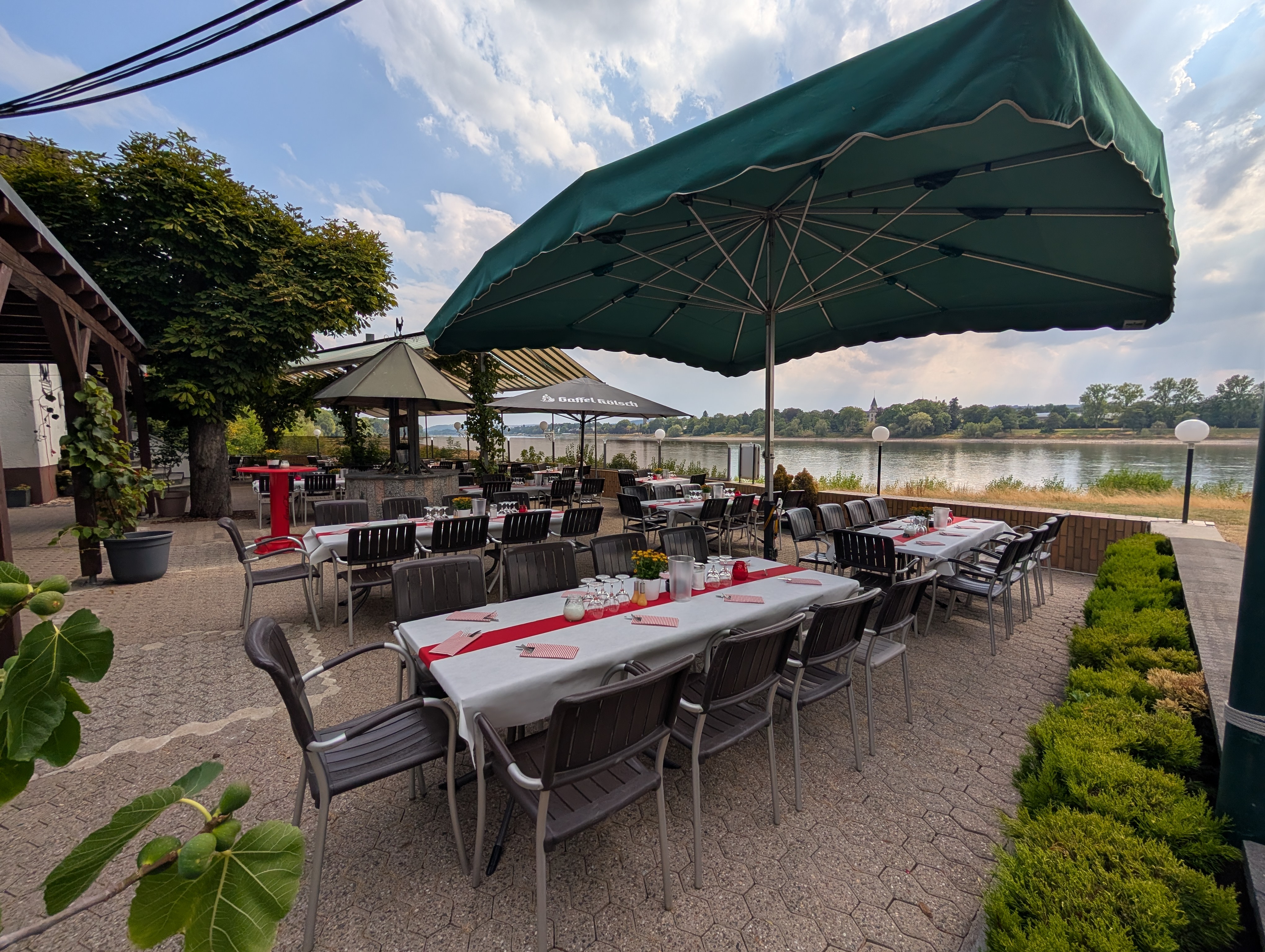 Gedeckte Tische auf der Rheinterrasse unter großen Sonnenschirmen mit Blick auf den Rhein